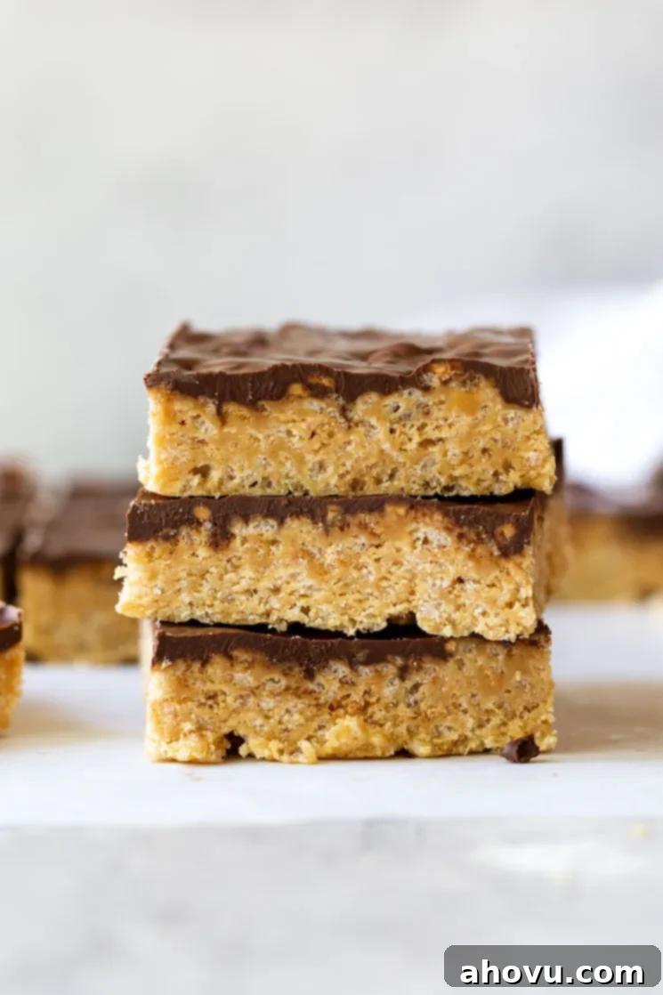 Classic Scotcheroos 2 A stack of three Scotcheroos on a rustic gray surface with more in the background, showcasing the layers of peanut butter rice krispie base and chocolate butterscotch topping.