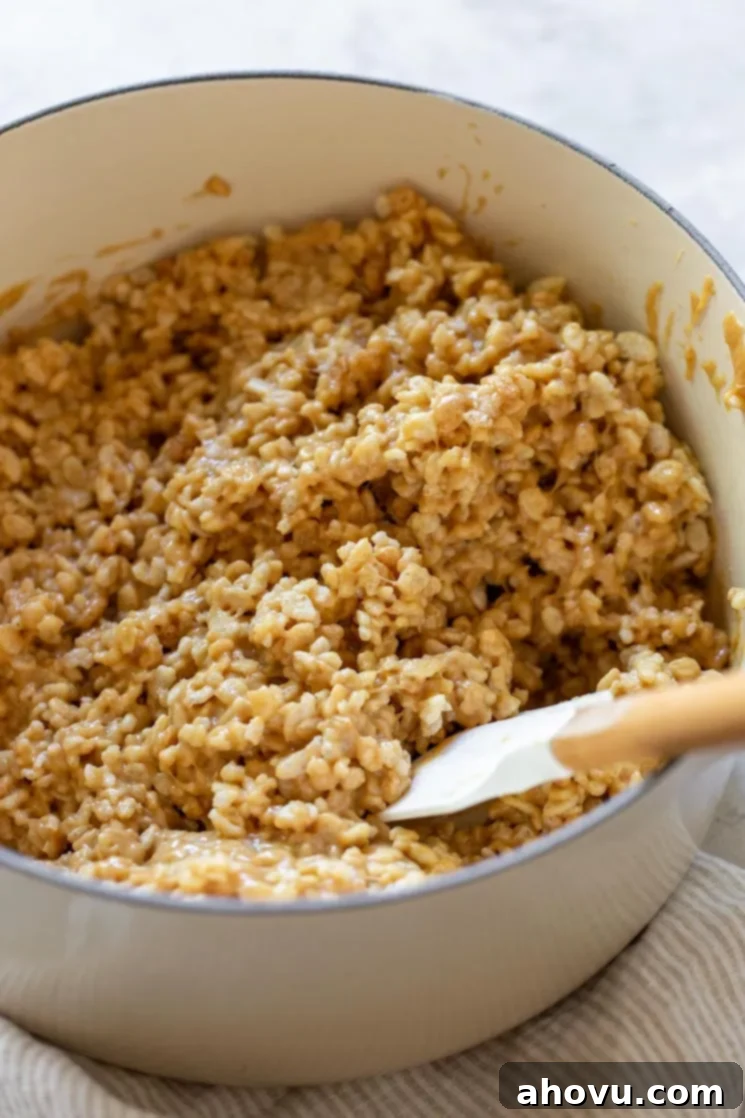 Classic Scotcheroos 4 A white saucepan filled with crispy rice cereal, being mixed with a melted peanut butter mixture to form the base of Scotcheroos.