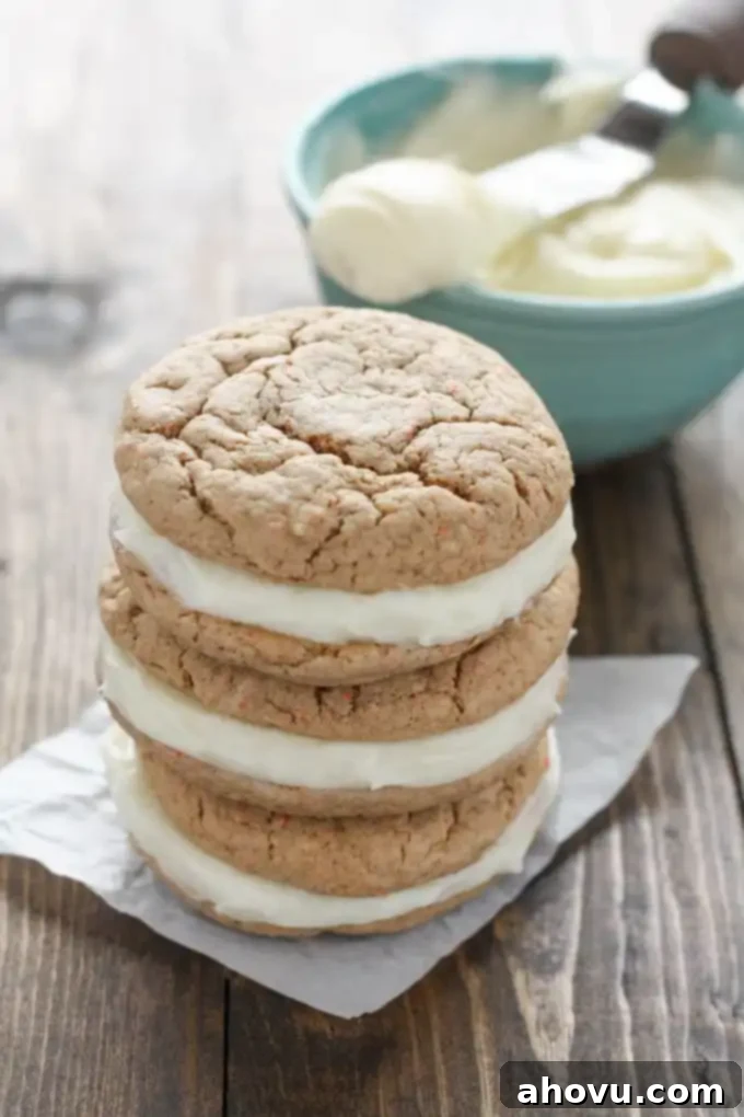 Carrot Cake Whoopie Pies 3 A close-up shot of three assembled carrot cake mix cookies with a thick, creamy layer of cream cheese filling in between, stacked neatly. A bowl of the delicious frosting rests in the background, out of focus.