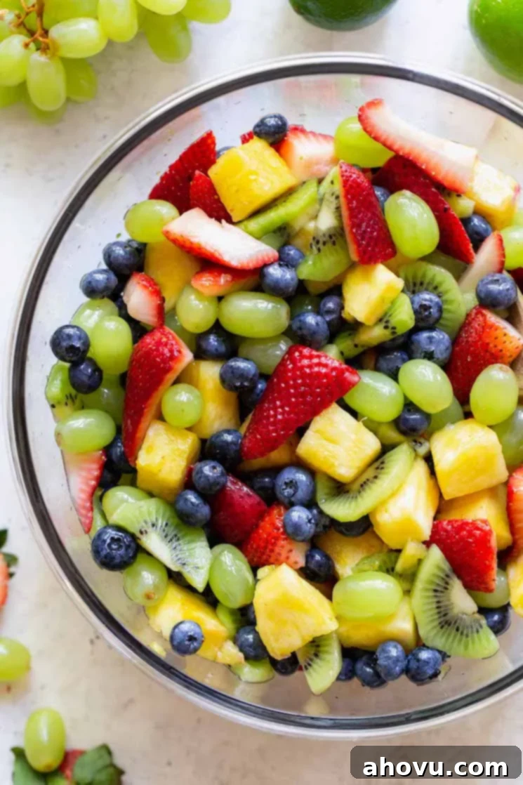 A vibrant glass bowl showcasing a beautifully arranged fruit salad, artfully placed on a rustic gray surface. Surrounding the bowl are additional pieces of fresh, colorful fruit, enhancing the visual appeal of the healthy dish.