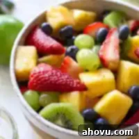 A white bowl filled with fresh fruit salad, topped with mint leaves for garnish, ready to be enjoyed.
