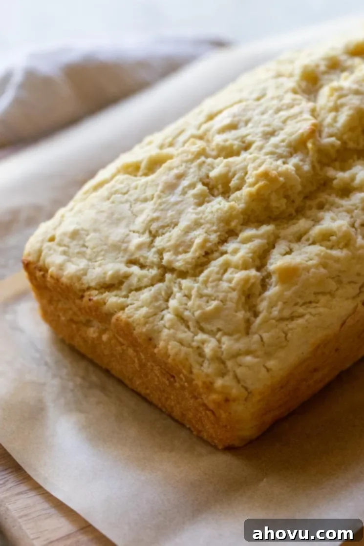 A perfectly baked loaf of golden-brown beer bread resting on a rustic wood cutting board to cool, steam gently rising.