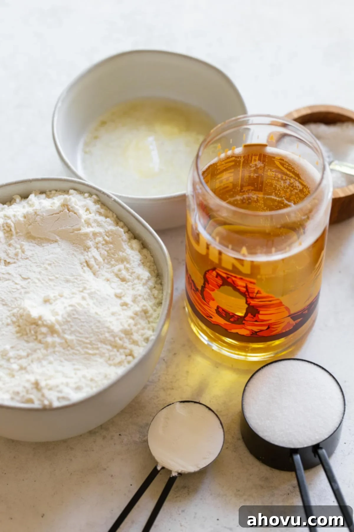 The six essential ingredients for making beer bread, including flour, sugar, baking powder, salt, butter, and beer, neatly arranged on a rustic gray surface.
