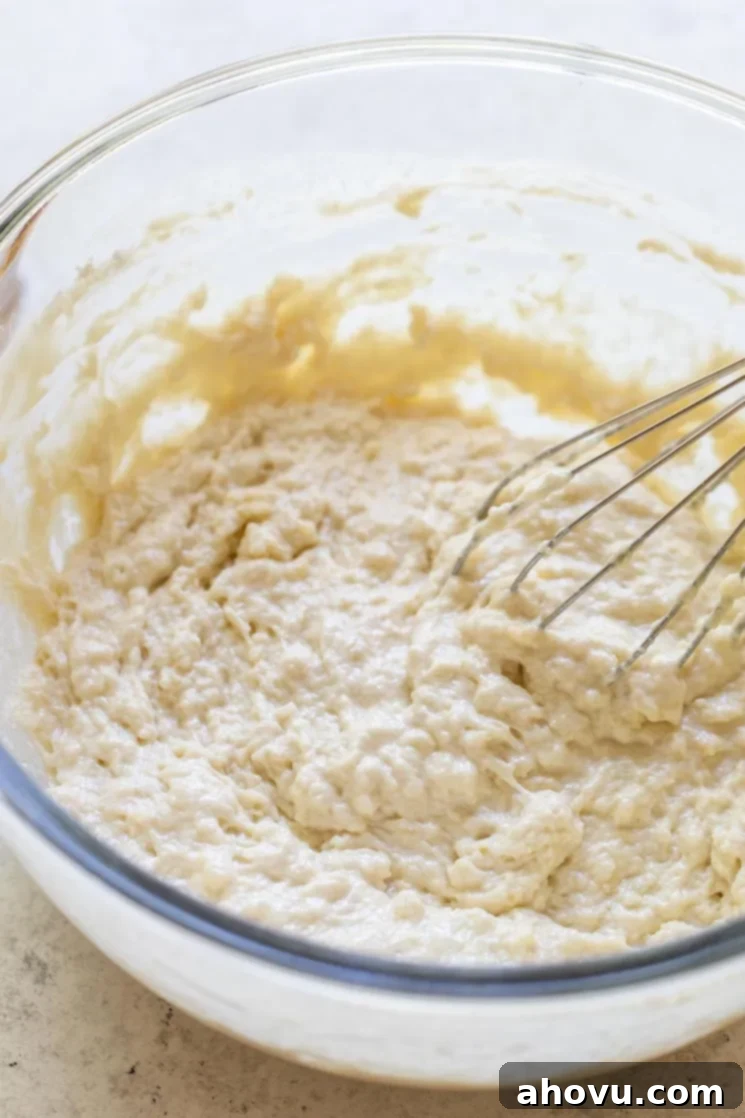 A glass bowl filled with the beer bread batter, freshly mixed with a metal whisk, showcasing its thick, consistent texture.