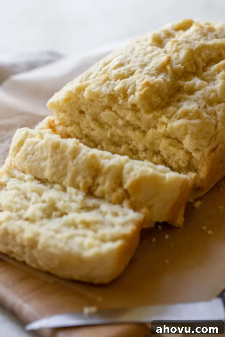 A freshly baked loaf of beer bread sliced on a wooden cutting board, revealing its tender, airy texture and golden crust.