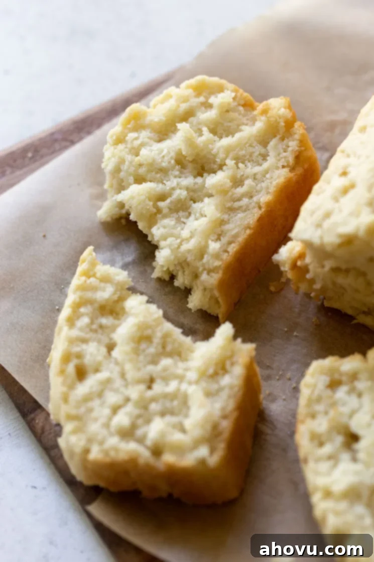A torn slice of beer bread resting on a wooden cutting board, revealing its soft interior, with the rest of the loaf blurred in the background.