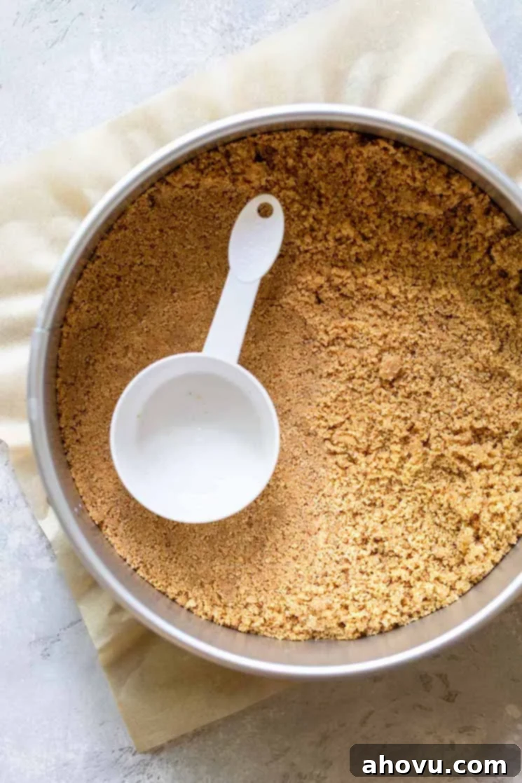 A springform pan holding graham cracker crumbs being pressed down for the crust.