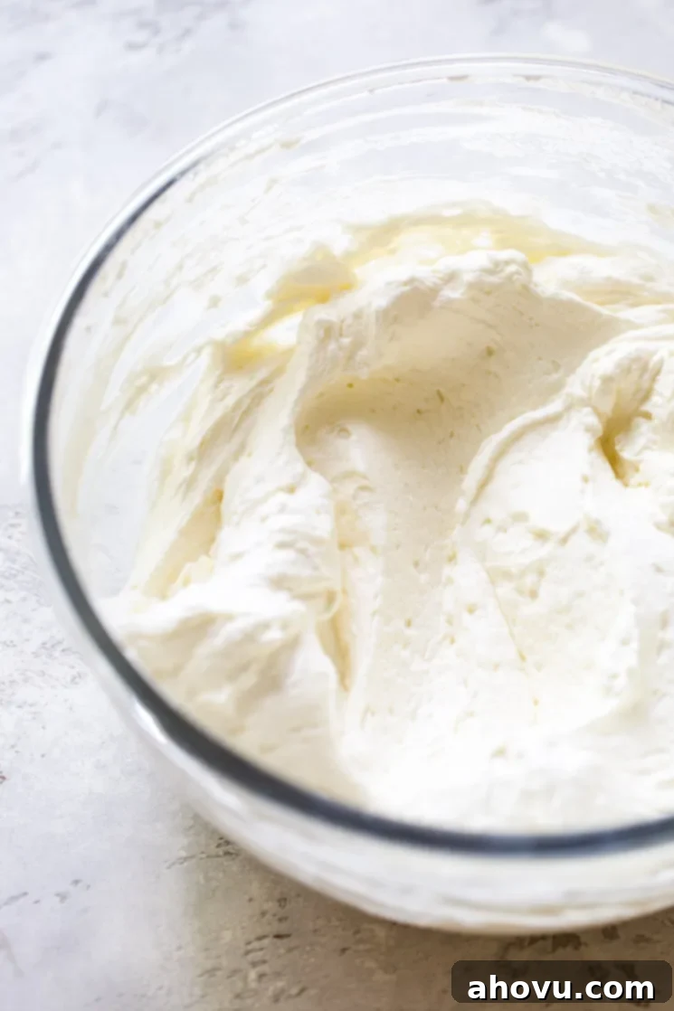 The no-bake cheesecake ingredients mixed up in a glass mixing bowl on top of a rustic gray surface. 