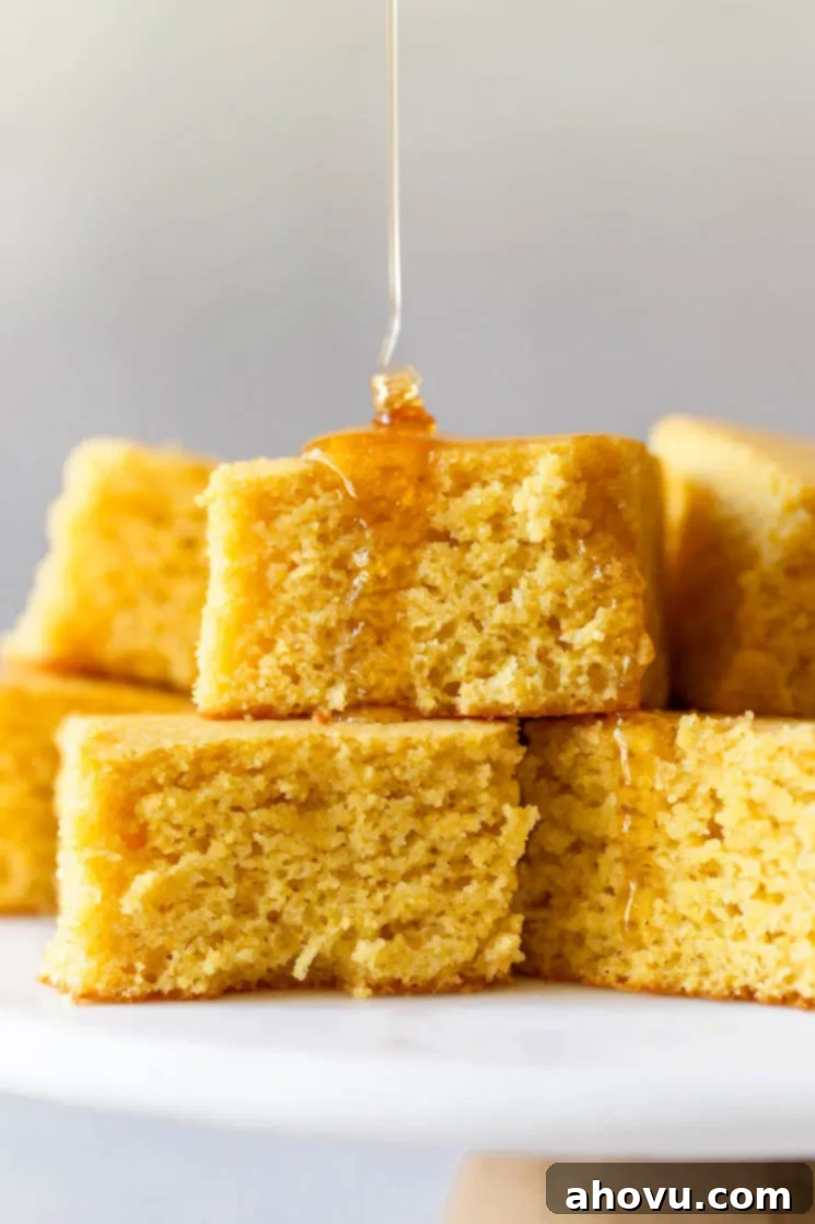 A stack of golden cornbread squares drizzled with honey, resting on an elegant marble cake stand.