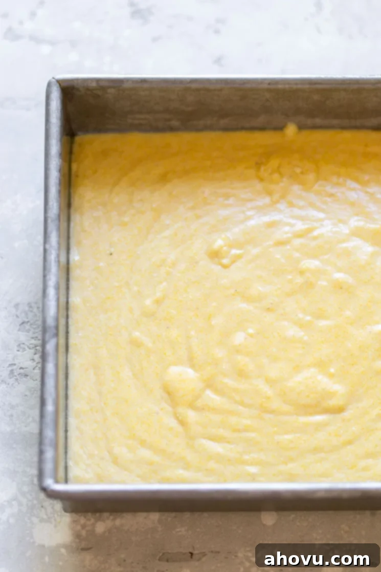 Smooth, golden cornbread batter freshly poured into an antique metal baking pan, perfectly prepped and ready for the oven to transform it into a delicious side dish.