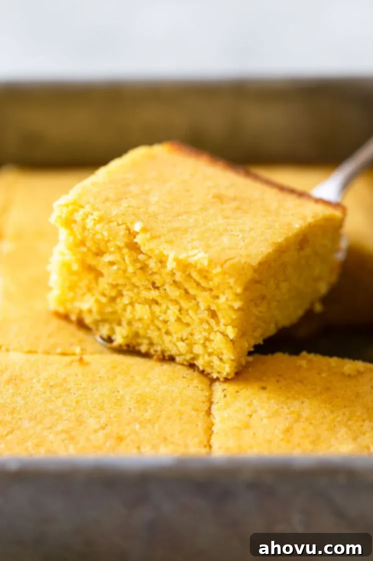 A finished pan of homemade cornbread, with one perfectly cut piece lifted and showcasing its soft, golden interior and wonderfully crispy crust.