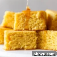 A stack of square cornbread slices with honey being drizzled on top, highlighting the golden color and moist texture.