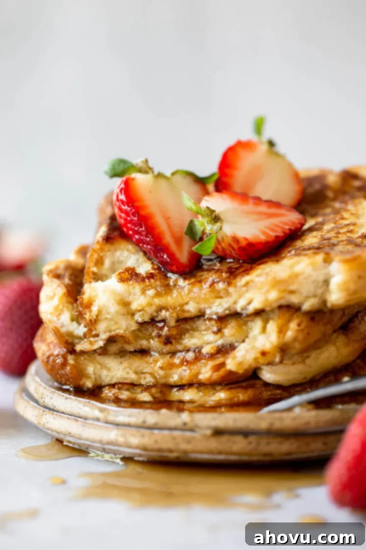 Fluffy French Toast Perfection 7 A plate holding French toast stacked up and topped with syrup and halved strawberries.