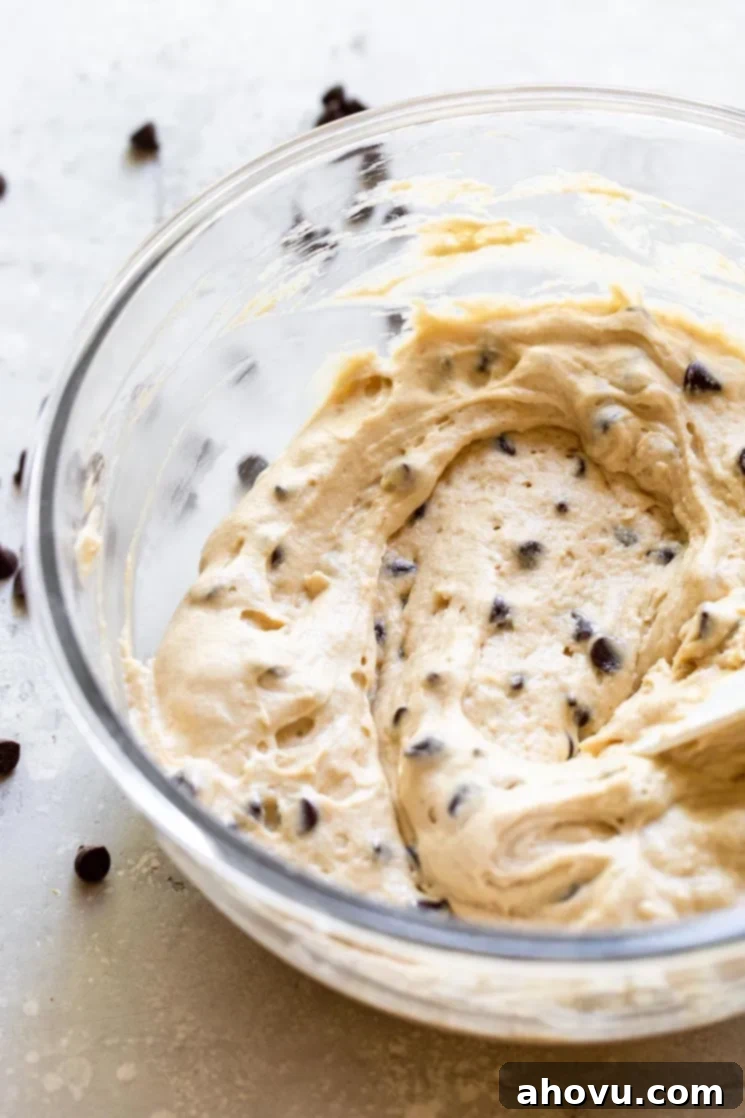 A clear glass bowl filled with rich, golden chocolate chip muffin batter, expertly mixed and ready for baking.