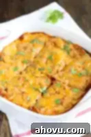 A slice of chicken enchilada casserole on a plate with melted cheese and sauce.