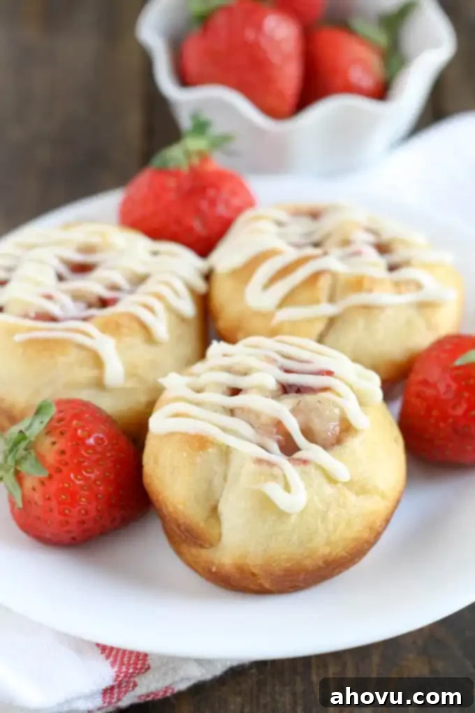 Luscious Strawberry Swirls 2 Three strawberry rolls topped with cream cheese frosting on a white plate with fresh berries.