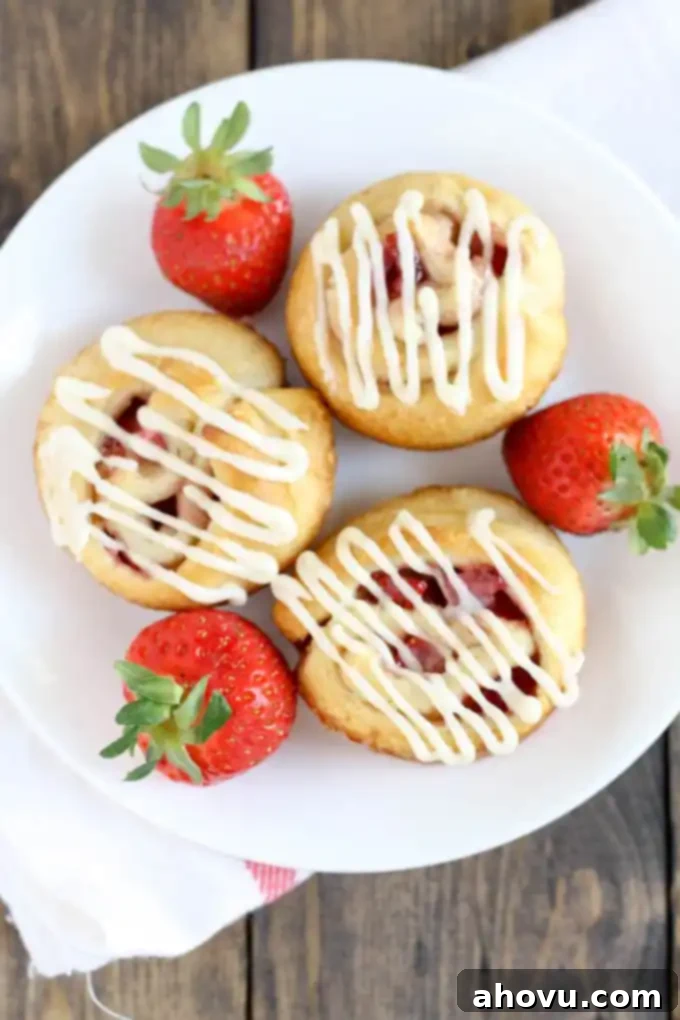Luscious Strawberry Swirls 3 Overhead view of three strawberry rolls and three fresh strawberries on a white plate.