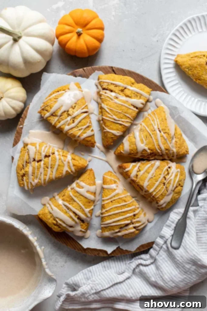 Spiced Pumpkin Scones 2 Pumpkin scones arranged in a circle on parchment paper topped with a maple cinnamon glaze, ready to be enjoyed.
