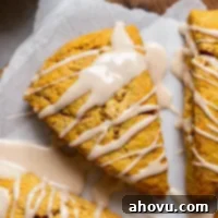 Spiced Pumpkin Scones 6 A perfectly baked pumpkin scone topped with maple cinnamon glaze resting on a piece of parchment paper.