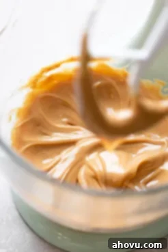 A glass mixing bowl containing softened unsalted butter and creamy peanut butter, partially blended to form a smooth base for the frosting.