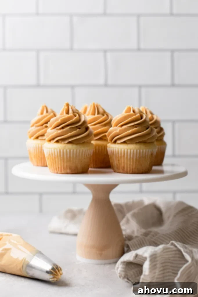A marble cake stand showcasing beautifully frosted vanilla cupcakes with peanut butter frosting, accompanied by a piping bag filled with more frosting, ready for decoration.
