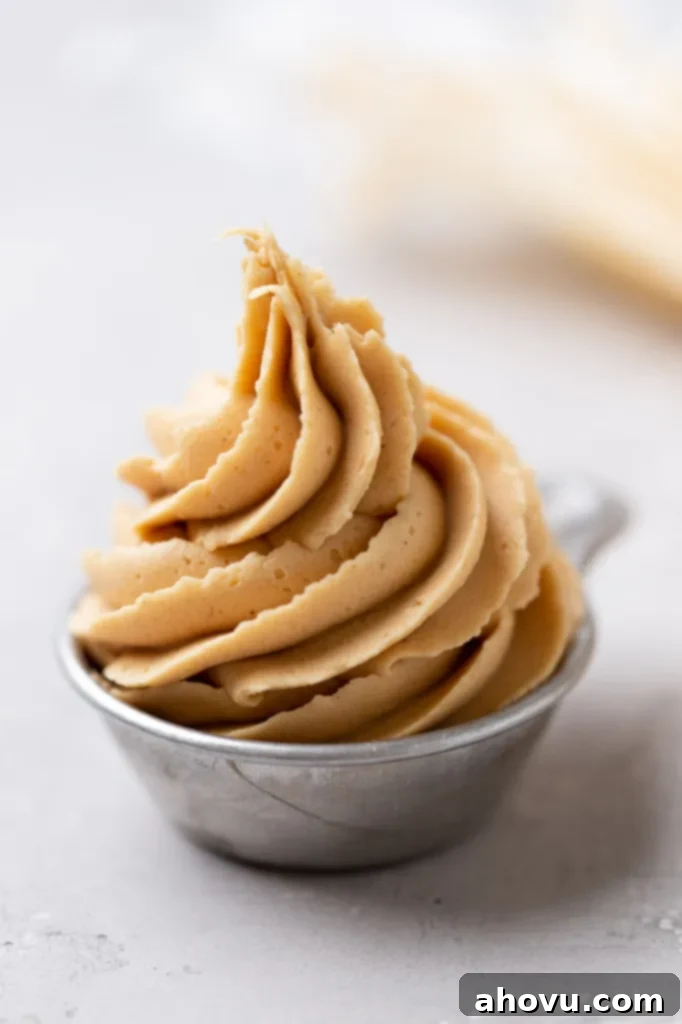 A small metal measuring cup filled to the brim with smooth, creamy peanut butter frosting, ready to be used or tasted.