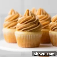 A marble cake stand holding several vanilla cupcakes topped with creamy peanut butter frosting.