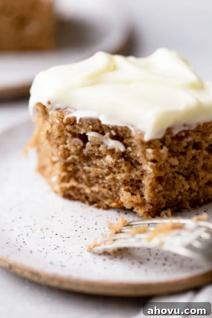 Golden Spiced Comfort 2 A single slice of perfectly moist homemade spice cake topped with creamy cream cheese frosting on a speckled white plate, with a bite playfully taken out, highlighting its tender texture.