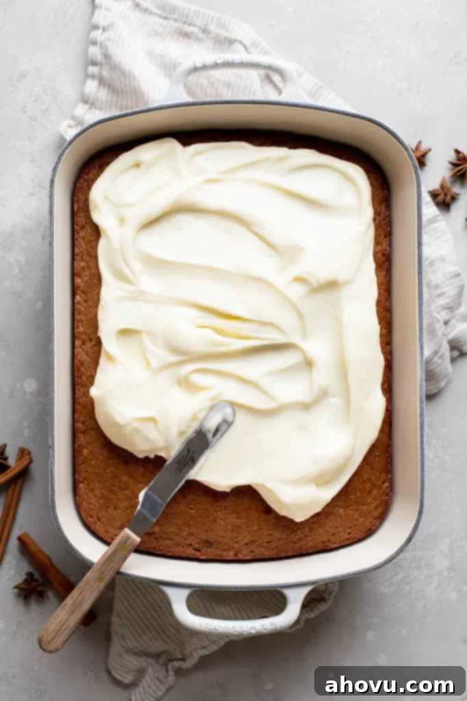 Golden Spiced Comfort 4 A rich, homemade spice cake freshly baked in a 9x13 inch pan is being generously frosted with smooth, tangy cream cheese frosting using an offset spatula.