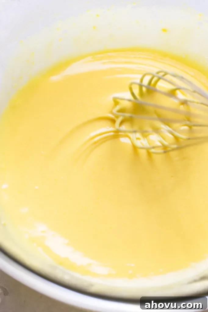 Egg yolk mixture being whisked in a glass bowl.