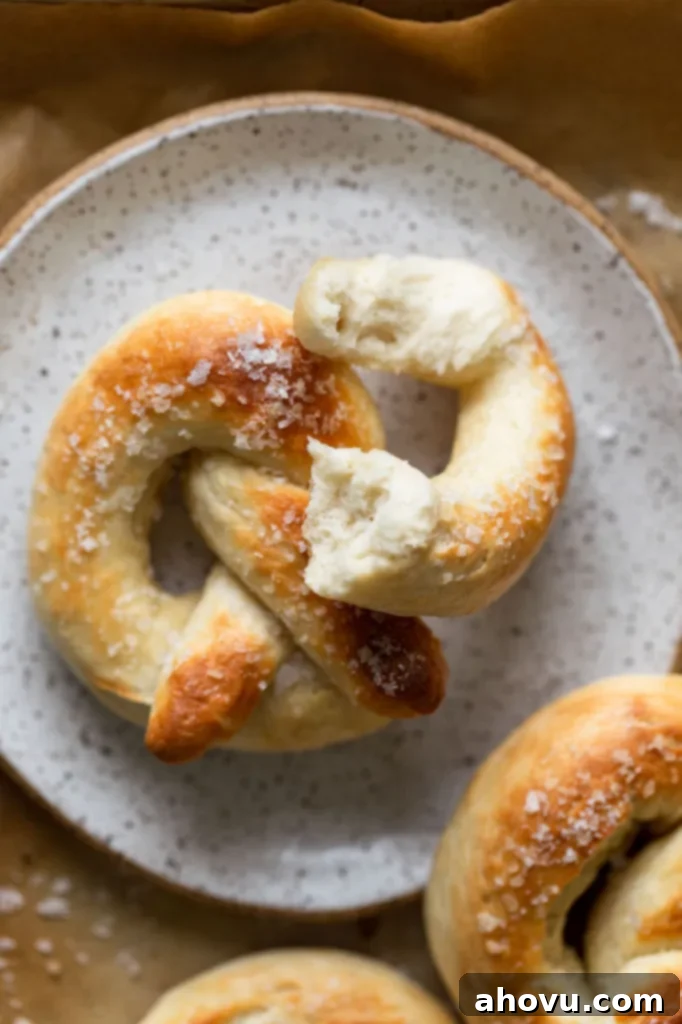 A homemade soft pretzel on a speckled white plate. A piece of the pretzel has been torn off. 