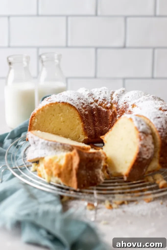 Half of a beautifully baked cream cheese pound cake on a wire rack, with three slices ready to serve. Two vintage milk bottles stand in the background, hinting at a cozy, homemade charm. The cake boasts a golden-brown crust and a tender crumb.