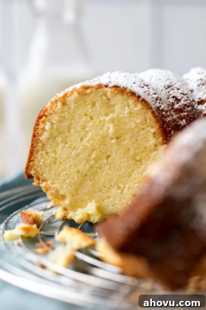A close-up side view of a perfectly sliced cream cheese pound cake, showcasing its incredibly moist and tender crumb. In the softly blurred background, milk bottles add a rustic, homely touch to the scene.