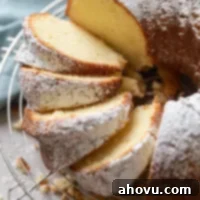 Overhead view of a cream cheese pound cake dusted with powdered sugar on a wire rack. Part of the cake has been sliced.