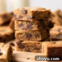 A stack of four chocolate chip cookie bars on a wood serving board. More cookie bars surround the stack.