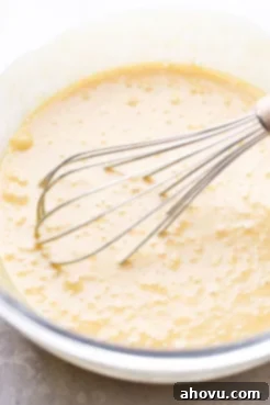 A glass mixing bowl filled with the wet ingredients being whisked together.