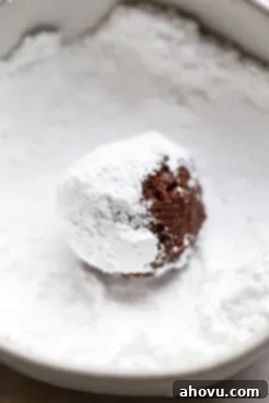 A single ball of cookie dough being rolled in powdered sugar.
