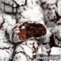 A batch of chocolate crinkle cookies with one cookie having a bite taken out of it.