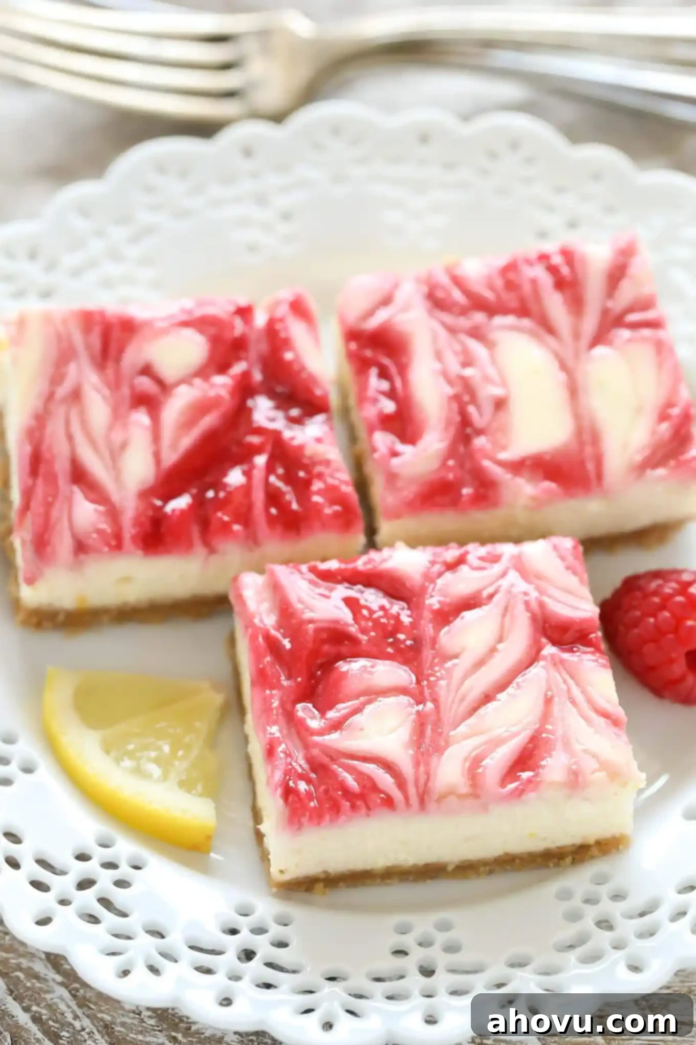 Three lemon raspberry cheesecake bars on a white dessert plate. 