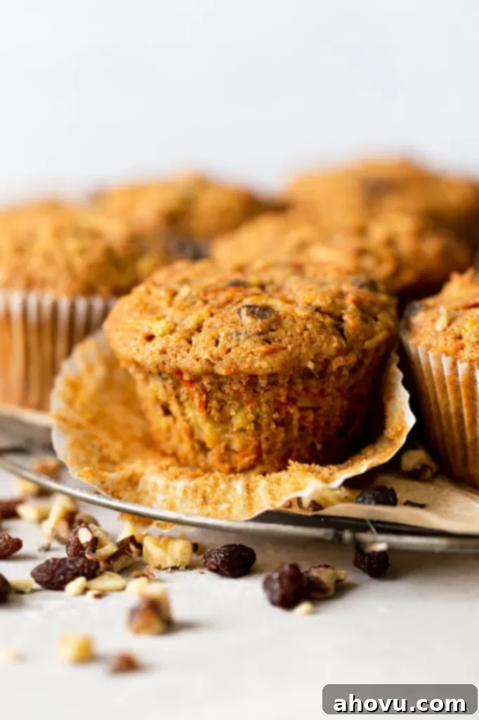 Side view of raisin apple carrot muffins on a wire cooling rack. The front muffin has had the paper liner pulled down. 