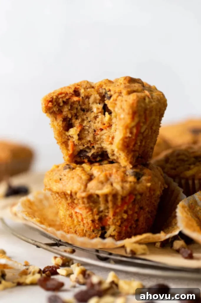 Two morning glory muffins stacked on top of each other, on a wire rack. The top muffin has a big bite missing. 
