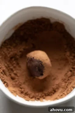 A perfectly rolled homemade chocolate truffle being coated in a generous layer of unsweetened cocoa powder, creating a classic finish.