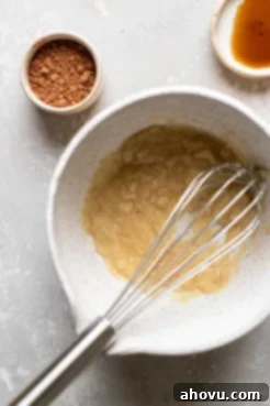 Melted butter and sugar in a mixing bowl with a whisk. A small dish of cocoa powder and vanilla extract sit on the side.