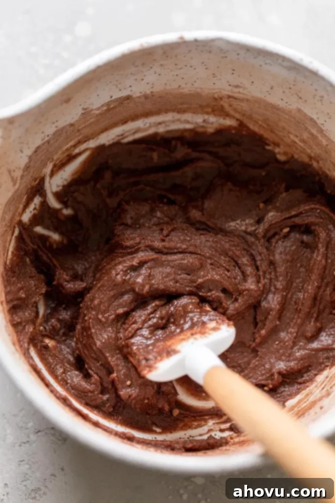 Decadent Mug Brownie 4 Overhead view of a mixing bowl filled with brownie batter. A rubber spatula is also in the bowl.