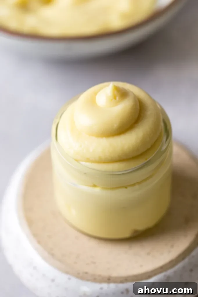 Perfect Homemade Pastry Cream 2 A small glass jar filled with luscious vanilla pastry cream, resting on an overturned bowl, with more creamy pastry cream visible in the background, highlighting its rich texture.