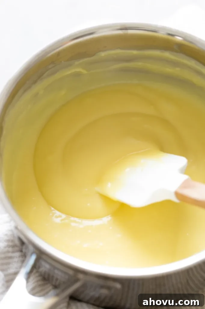 Perfect Homemade Pastry Cream 4 A saucepan filled with warm, thick pastry cream, with a rubber spatula resting inside after stirring, showcasing its rich consistency.