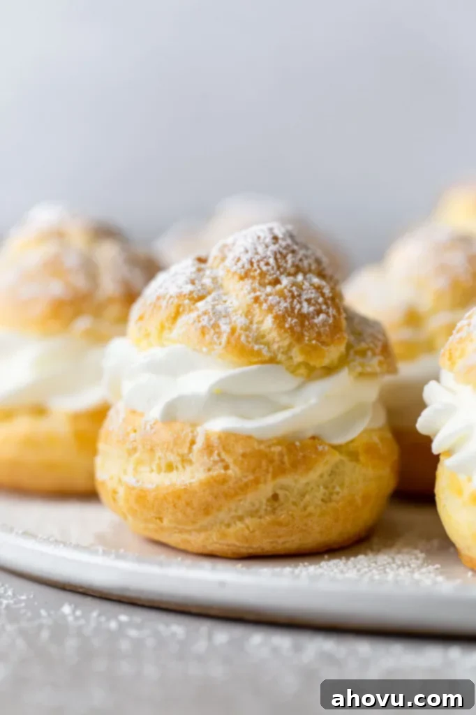 Side view of homemade cream puffs filled with whipped cream on a white plate. 