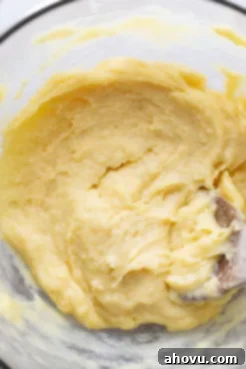 Choux pastry dough in a large glass bowl with a wooden spoon.