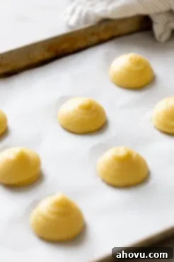 Choux pastry dough piped onto a parchment paper-lined baking tray.