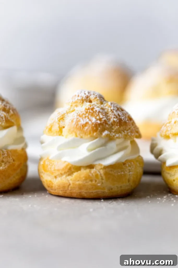 Side view of filled cream puffs lined up on a countertop. More cream puffs rest on a plate in the background.